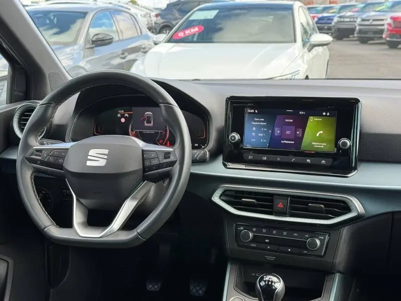 Vue intérieure du poste de conduite du SEAT Arona 2025 avec volant multifonction, écran tactile central et levier de vitesse manuel.