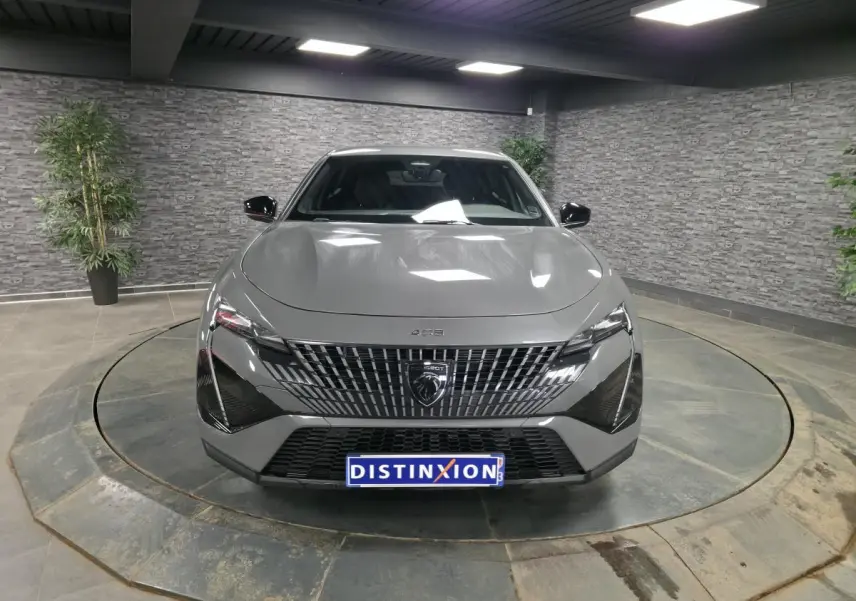 Vue frontale d'une Peugeot 408 gris métallisé avec calandre verticale et phares LED distinctifs en intérieur showroom.