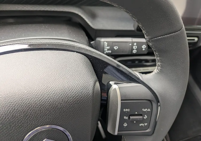 Gros plan sur le volant noir du Citroën C3 Aircross 2026, avec commandes intégrées et détails de la commande d’essuie-glace en arrière-plan.