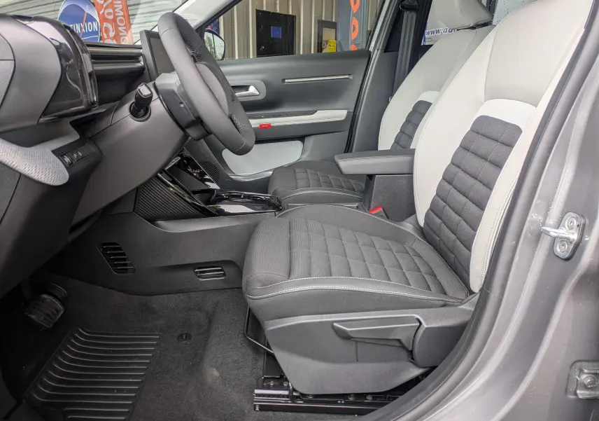 Vue intérieure côté conducteur du Citroën C3 Aircross 2026, sièges bicolores gris clair et foncé avec console centrale noire brillante.