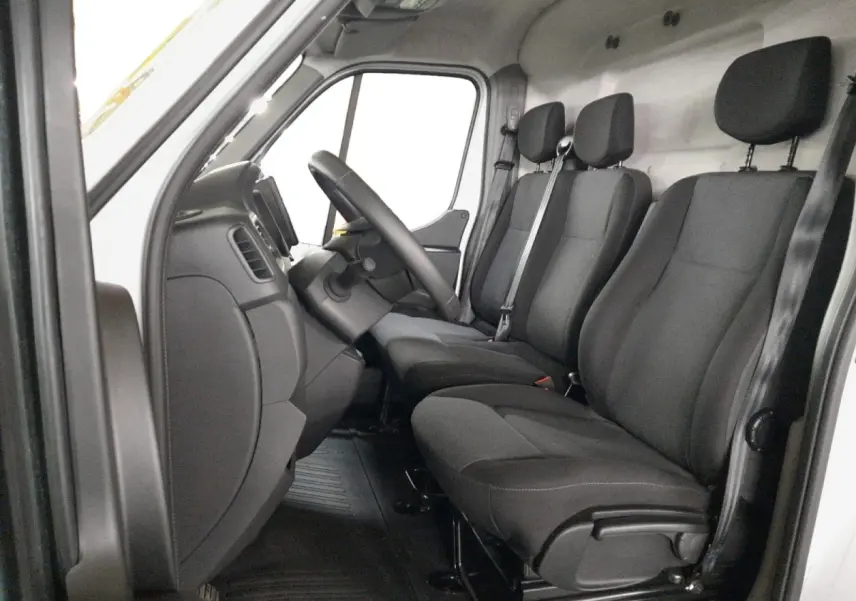Vue intérieure côté conducteur du Renault Master 2024 blanc, montrant les sièges avant en tissu noir et le volant réglable.