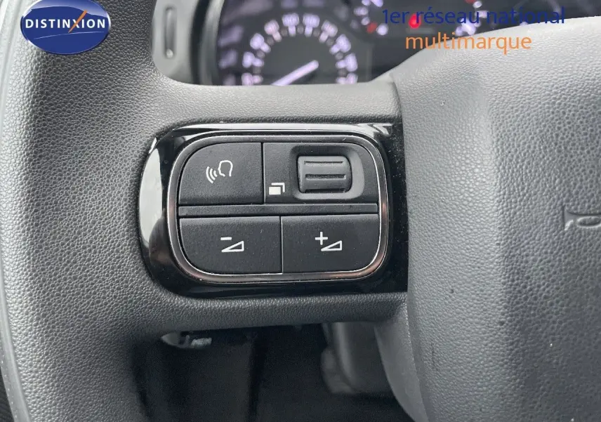 Gros plan sur les commandes de volume et téléphone intégrées au volant gris d'une Citroën C3 2023.