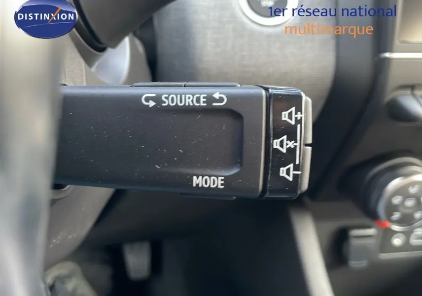 Gros plan sur la commande au volant de la Renault Clio noire étoile métal, montrant les boutons source et mode audio.