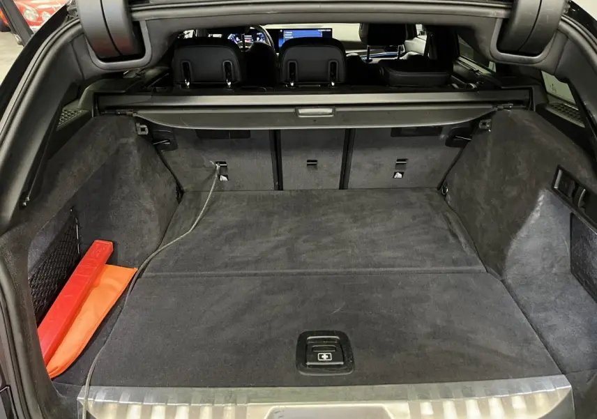 Coffre ouvert vu de l'arrière d'une BMW Série 3 Touring 320e noire, avec tapis et cache-bagages gris foncé.