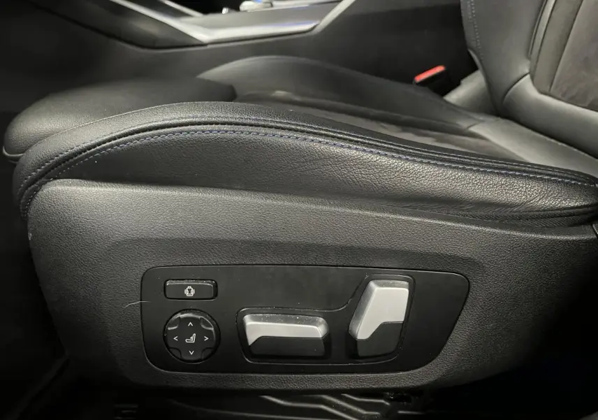 Gros plan sur les commandes électriques noires et argentées de l'appui lombaire côté conducteur d'une BMW Série 3 Touring noire.