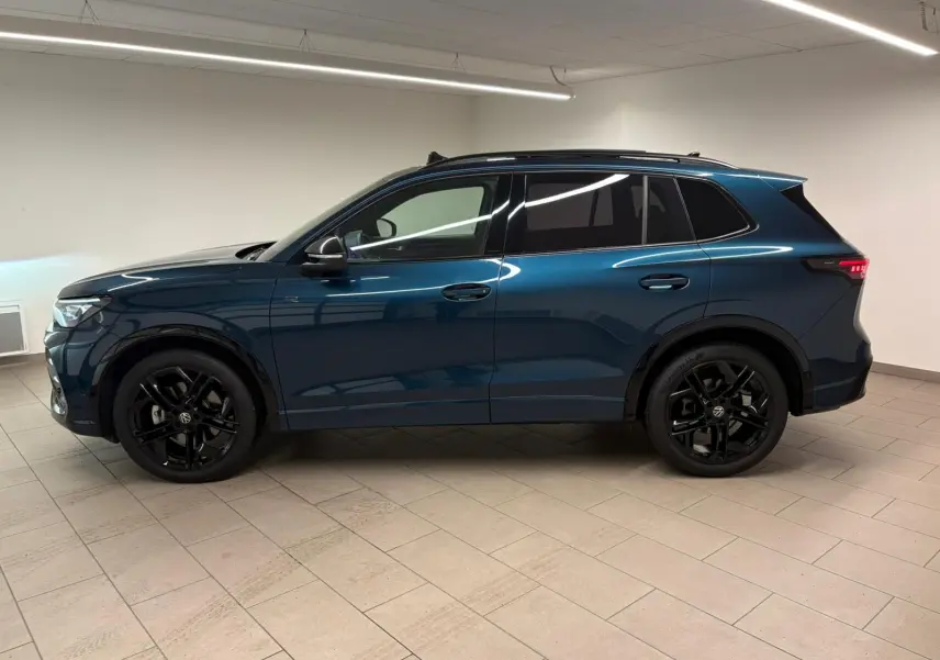 Vue de profil côté gauche du Volkswagen Tiguan 2024 en Nightshade Blue avec jantes noires et vitres surteintées.