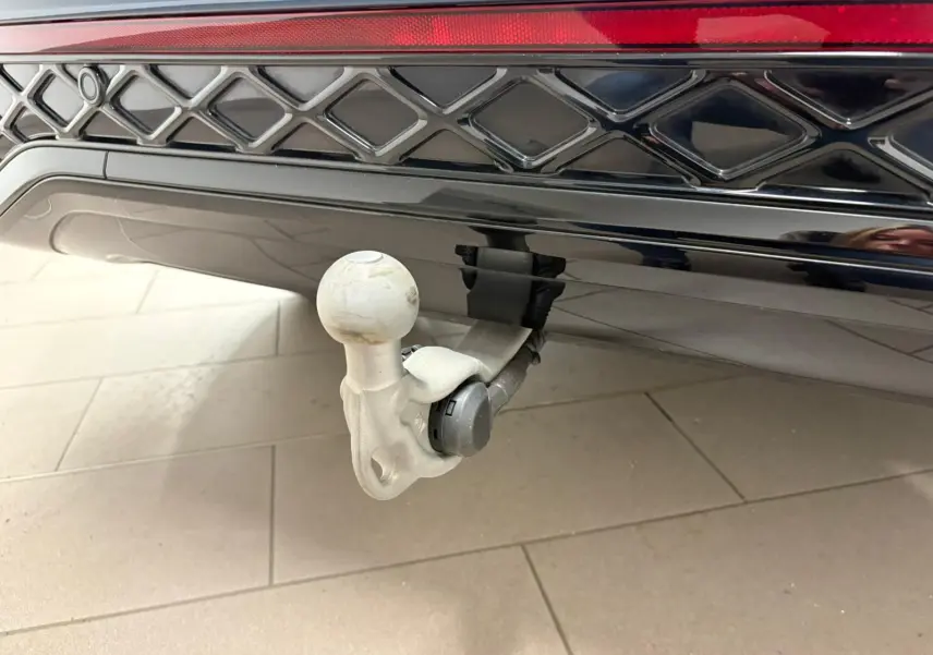 Gros plan sur le crochet d'attelage escamotable électrique du Volkswagen Tiguan Nightshade Blue, partie arrière noire brillante.