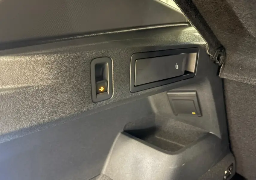 Détail intérieur du coffre du Volkswagen Tiguan 2024, montrant les commandes de rabattement des sièges en plastique noir.