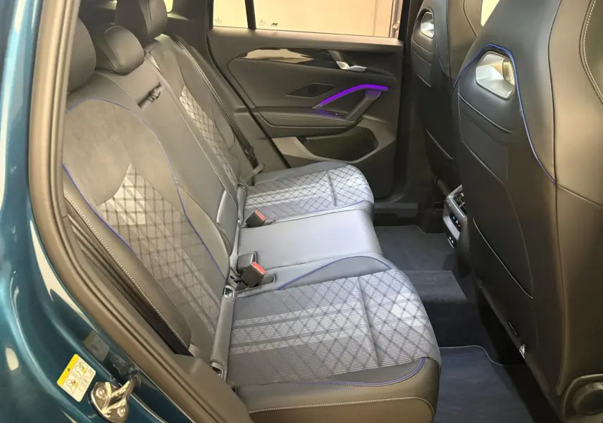 Vue intérieure côté gauche des sièges arrière du Volkswagen Tiguan 2024 en Nightshade Blue avec surpiqûres bleues et éclairage d'ambiance violet.