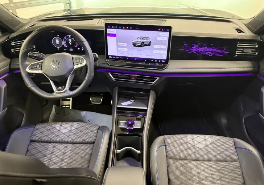 Vue intérieure avant du Volkswagen Tiguan 2024 avec tableau de bord numérique, écran tactile central et éclairage d'ambiance violet.
