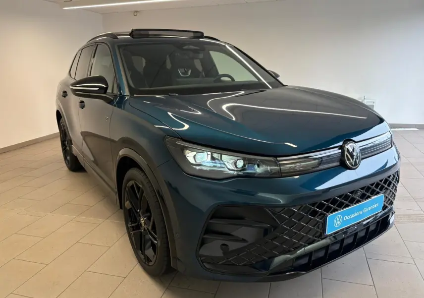 Volkswagen Tiguan 2024 Nightshade Blue en 3/4 avant droit, jantes noires et calandre R-Line noire visible.