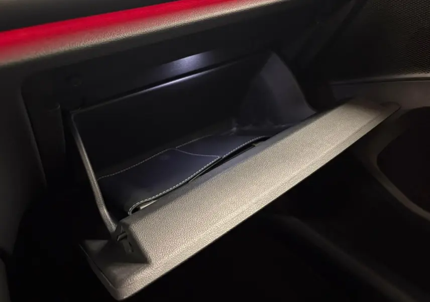 Gros plan sur la boîte à gants ouverte du Volkswagen Tiguan 2024, intérieur noir avec éclairage rouge ambiant.