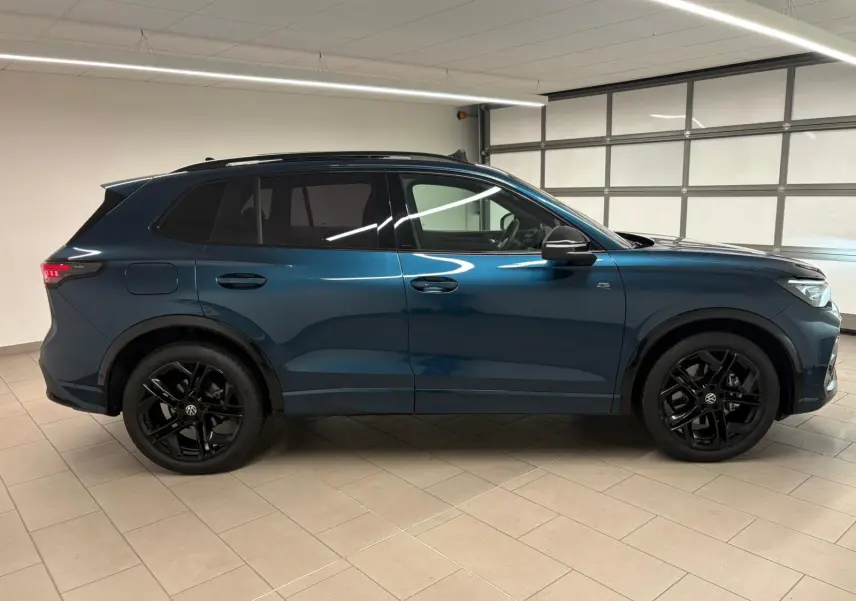 Vue de profil côté gauche d'un Volkswagen Tiguan 2024 en Nightshade Blue avec jantes noires et toit ouvrant panoramique.