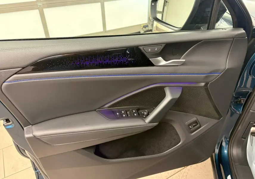 Vue intérieure côté gauche de la porte avant d’un Volkswagen Tiguan Nightshade Blue avec éclairage d’ambiance violet et surpiqûres bleues.