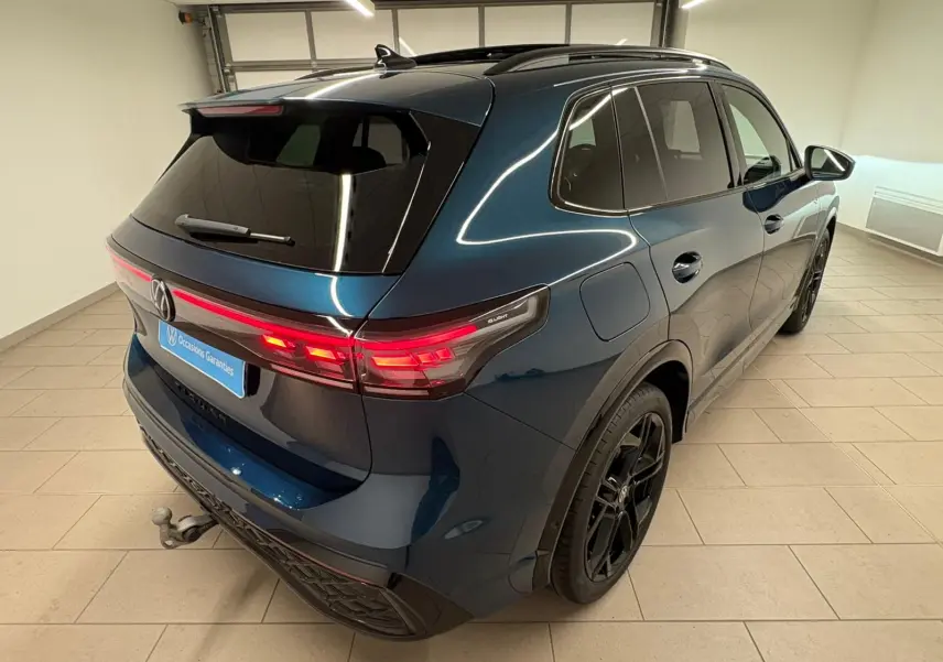 Vue 3/4 arrière droite du Volkswagen Tiguan 2024 Nightshade Blue avec jantes noires et attelage escamotable.