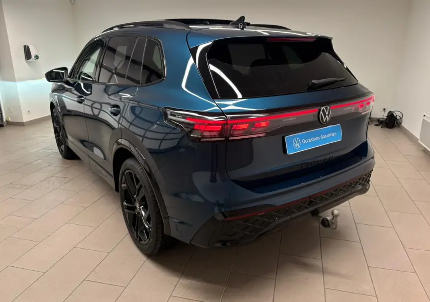Vue 3/4 arrière du Volkswagen Tiguan 2024 en Nightshade Blue avec jantes noires et attelage escamotable.