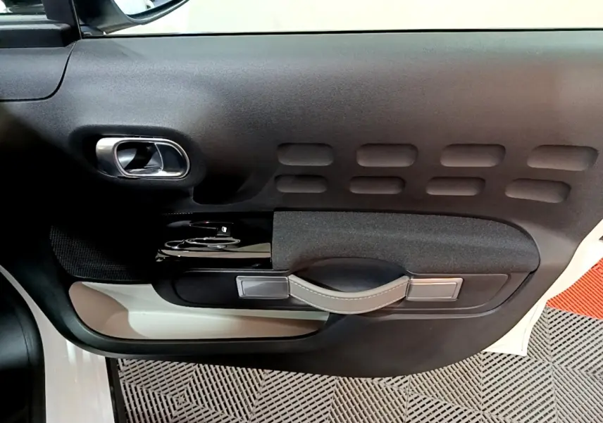 Vue rapprochée de la porte côté conducteur d'une Citroën C3 blanche, avec poignée intérieure en cuir et inserts noirs.