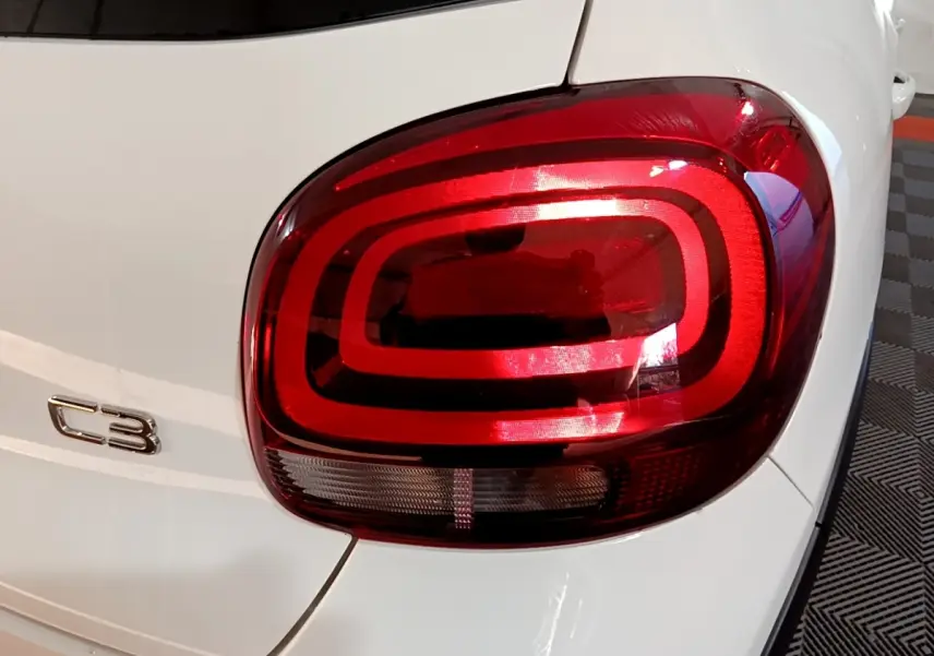 Gros plan sur le feu arrière droit rouge et le logo C3 d'une Citroën C3 blanche vue de l'arrière.