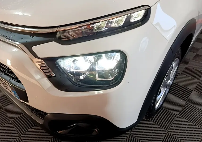 Gros plan sur l'avant droit d'une Citroën C3 blanche, mettant en valeur ses phares LED et son pare-chocs noir.