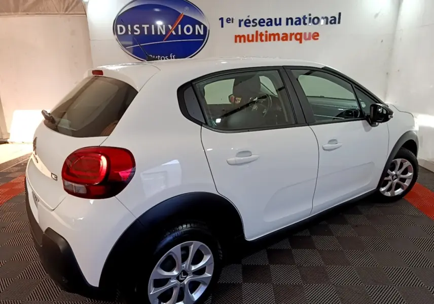 Vue 3/4 arrière droite d'une Citroën C3 blanche 2020 avec arches de roues noires et jantes alliage en showroom.