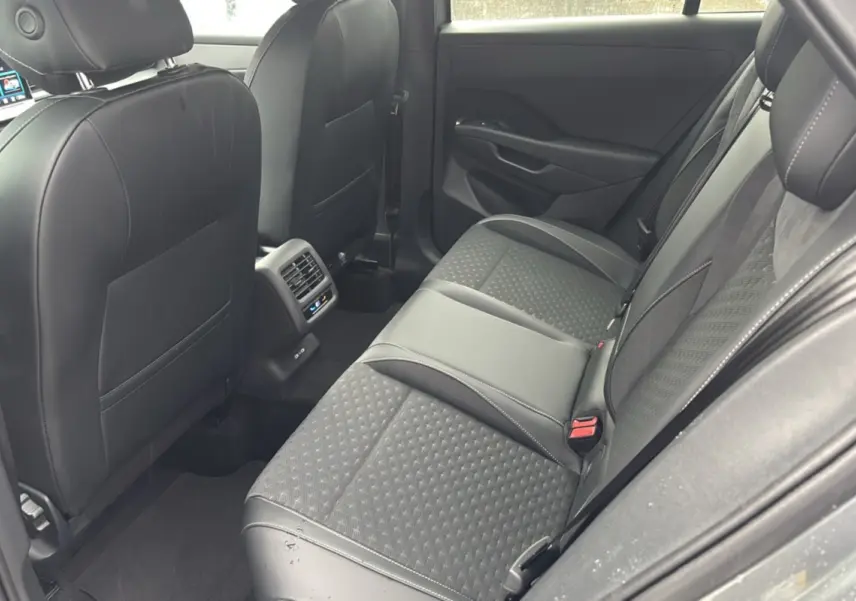 Vue intérieure arrière droite du Volkswagen T-Roc gris loup, montrant la banquette tissu et cuir avec accoudoir central.