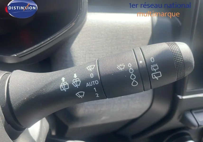 Gros plan sur la manette des essuie-glaces à l'intérieur d'une Renault Clio blanche, détails des pictogrammes visibles.