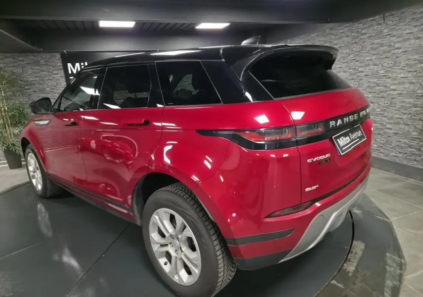 Vue 3/4 arrière droite du Range Rover Evoque rouge avec toit noir et jantes argentées en intérieur showroom.