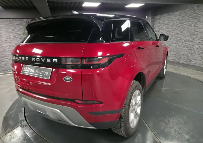 Vue 3/4 arrière droite d'un Range Rover Evoque rouge avec toit noir et jantes argentées dans un showroom.