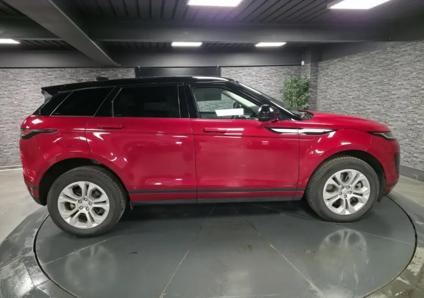 Vue de profil côté gauche d'un Range Rover Evoque rouge avec toit noir contrasté dans un showroom intérieur.