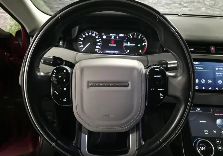 Vue rapprochée du volant noir et gris avec commandes intégrées du Range Rover Evoque rouge, tableau de bord digital en arrière-plan.