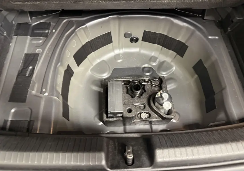 Vue plongeante sur le coffre ouvert d'une Volkswagen Polo gris cendre, montrant le logement de la roue de secours et les outils.