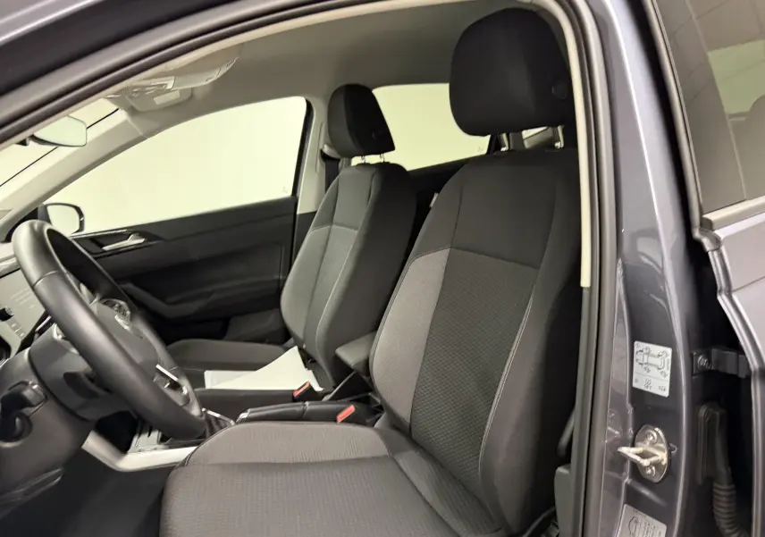 Vue intérieure côté conducteur de la Volkswagen Polo gris cendre 2025, sièges tissu noir et volant cuir multifonctions.