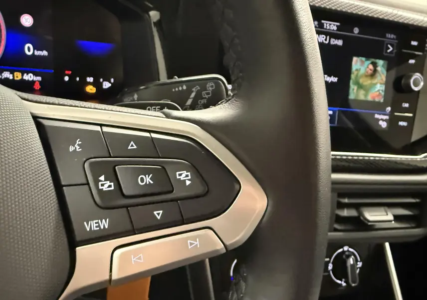 Vue rapprochée du volant cuir noir avec commandes multifonctions et écran tactile du tableau de bord d'une Volkswagen Polo gris cendre 2025.