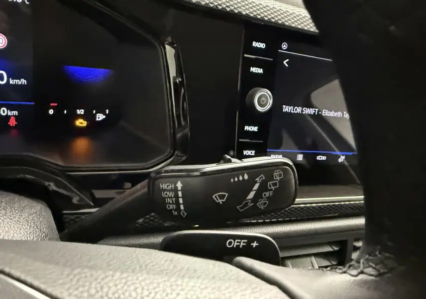 Gros plan intérieur sur la commande d’essuie-glace à gauche du volant d’une Volkswagen Polo gris cendre, avec écran tactile en arrière-plan.