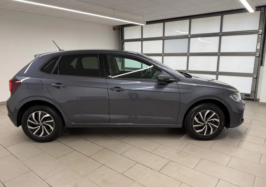Profil droit d'une Volkswagen Polo gris cendre 2025 avec jantes alliage bicolores et vitres surteintées en intérieur lumineux.