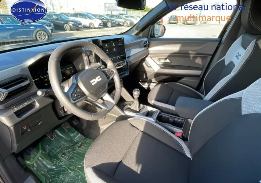 Intérieur avant du Dacia Duster 2026, vue côté conducteur, volant multifonction et sièges bi-ton gris et noir.