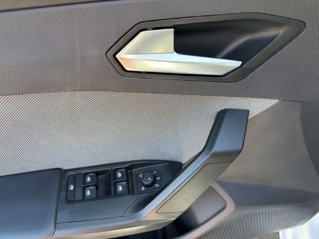 Détail de la porte côté conducteur du SEAT Leon blanc 2025, avec commandes électriques des vitres et poignée argentée.