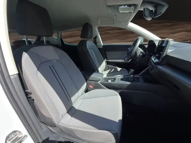 Vue intérieure côté conducteur de la SEAT LEON blanche 2025, montrant sièges tissu gris et tableau de bord avec écran tactile.