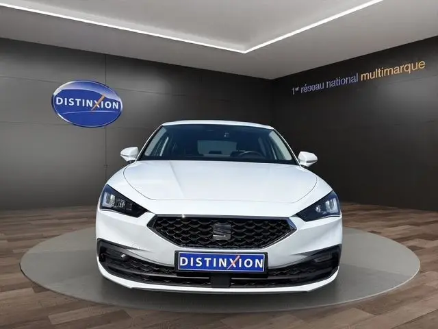 Vue de face d'une SEAT Leon blanche 2025 avec calandre noire et phares LED dans un showroom.