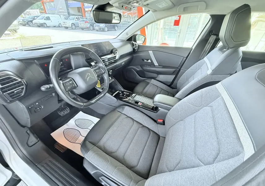 Vue intérieure côté conducteur de la Citroën C4 2023, sièges gris tissu et cuir, tableau de bord moderne avec volant multifonction.