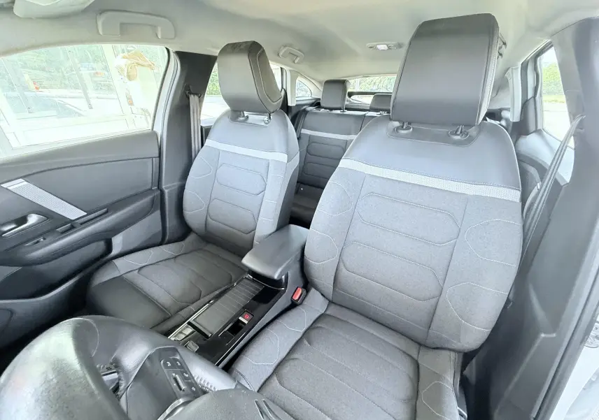 Vue intérieure avant de la Citroën C4 2023, sièges gris tissu avec appuie-têtes noirs et console centrale noire.