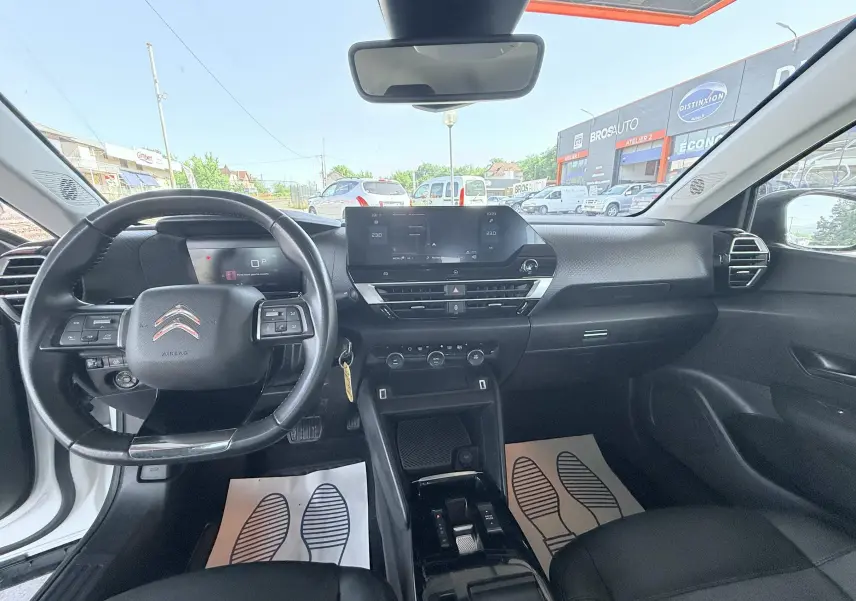 Vue intérieure avant de la Citroën C4 blanche 2023, tableau de bord noir avec écran tactile et volant multifonction.