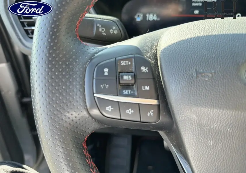 Gros plan sur le volant sport noir à surpiqûres rouges du Ford Kuga 2024 avec commandes intégrées.