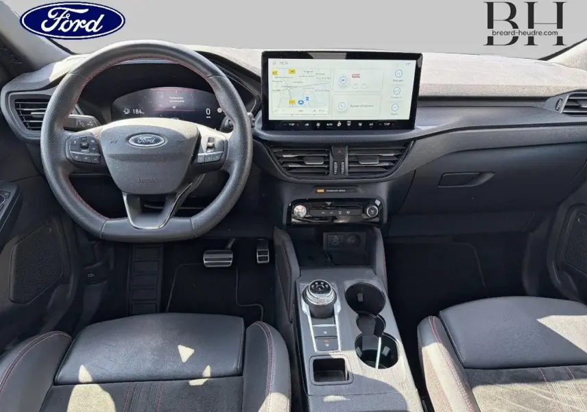 Vue intérieure frontale du Ford Kuga 2024, tableau de bord noir avec écran tactile central et volant multifonction.