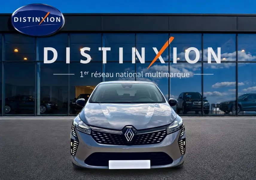 Vue frontale d'une Renault Clio V gris foncé 2025 avec calandre moderne et feux LED allumés devant un showroom Distinxion.