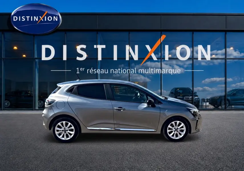 Profil droit d'une Renault Clio V gris foncé 2025, avec jantes alliage et vitres teintées, devant une vitrine Distinxion.