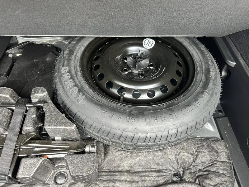 Roue de secours en acier noir avec cric et outils dans le coffre d'un Renault Arkana noir métal 2023.