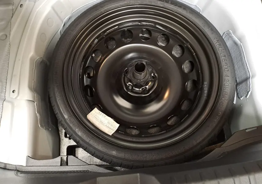 Roue de secours noire en acier dans le coffre d'une SEAT Ibiza blanc candy 2023, vue plongeante sur la roue.