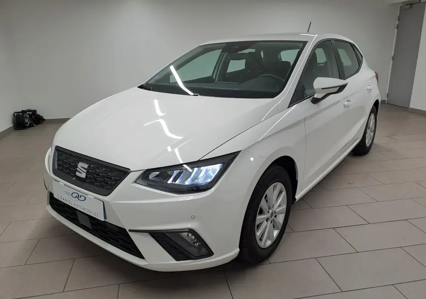 SEAT Ibiza 2023 blanc candy vue 3/4 avant droit avec phares allumés dans un showroom intérieur.