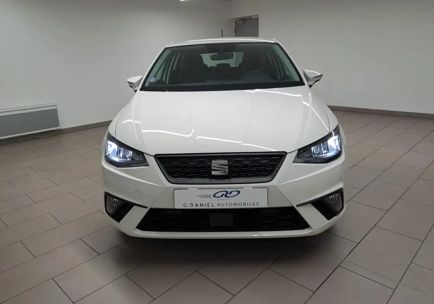Vue frontale d'une SEAT IBIZA blanc candy 2023 avec phares allumés dans un showroom intérieur.